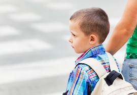 Junge mit Rucksack an der Hand eines Elternteils