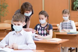 Lehrerin und Schüler*innen im Klassenraum Lehrerin und Schüler*innen mit Mund-und Nasenschutz im Klassenraum